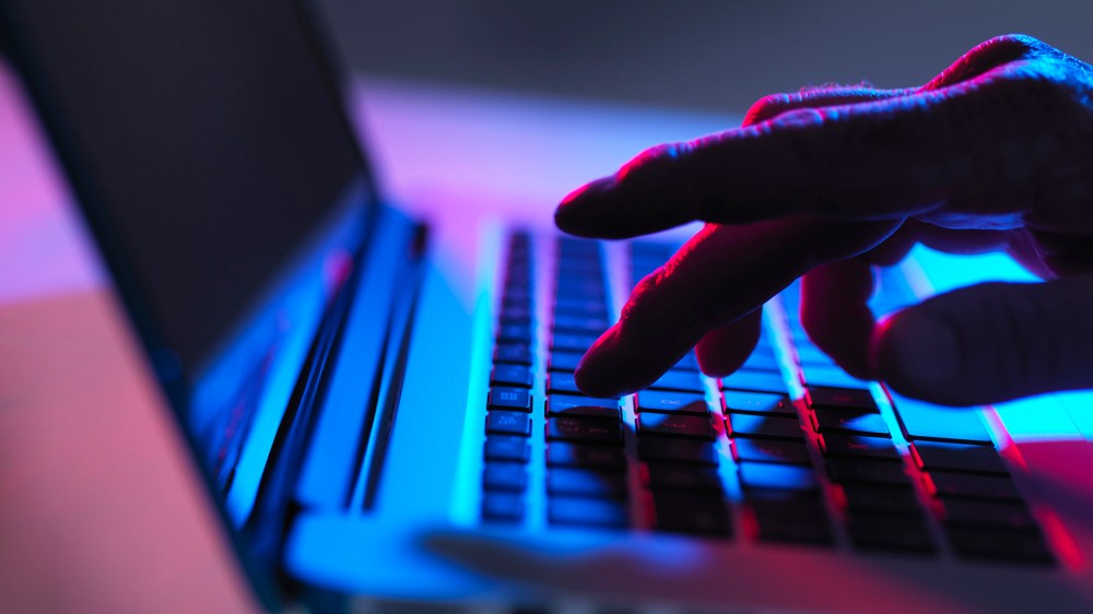 Image: Silhouette of male hand typing on laptop keyboard at night