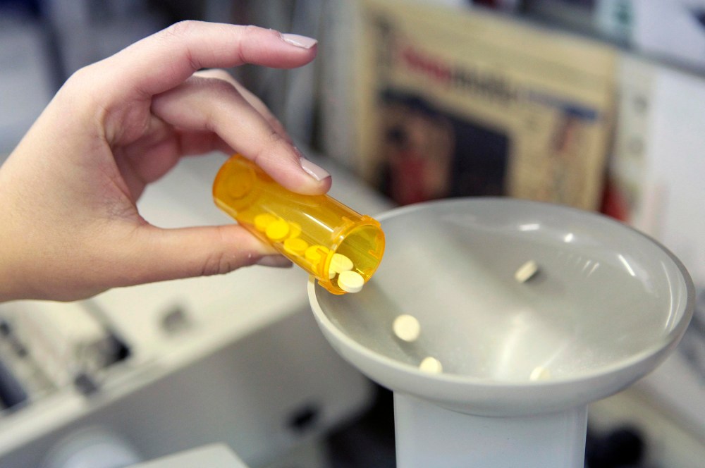 Image: A pharmacy employee dumps pills into a pill counting machine as she fills a prescription.