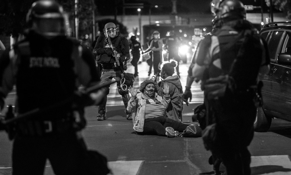 Image: Two protestors surrounded by armed police officials.