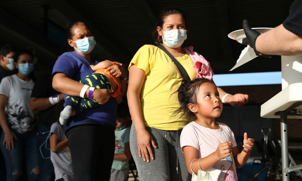 Image: A girl in a line reaches out for a plate of food at a bus station.