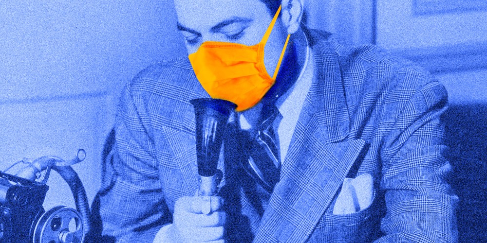 Photo illustration: A person wearing a suit and a protective mask speaking into a dictaphone.