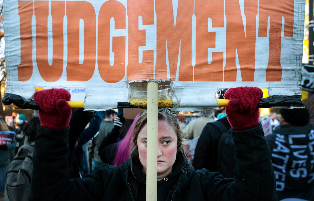 Image: A woman holding up a sign that reads,"Judgement".