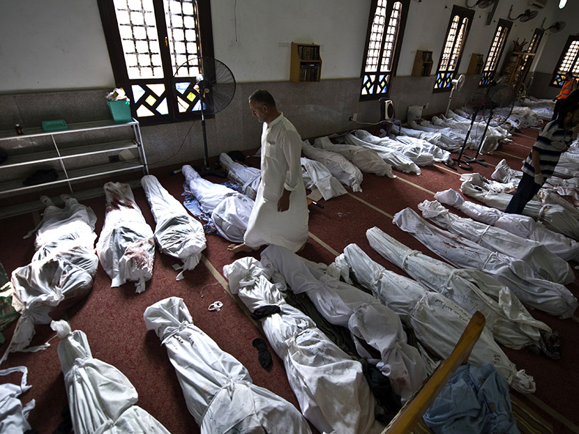 An Egyptian man walks between lines of bodies wrapped in shrouds at a mosque in Cairo on August 15, 2013, following a crackdown on the protest camps of supporters of ousted Islamist president Mohamed Morsi the previous day.  (Photo by Khaled Desouki...