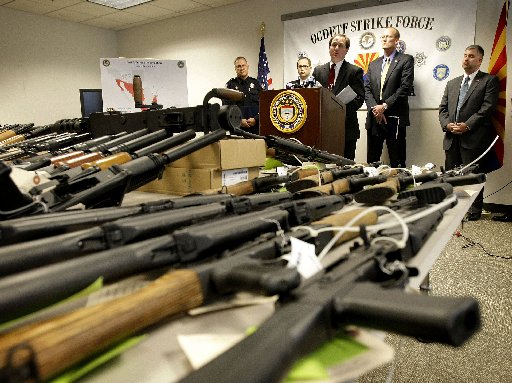 File Photo: United States Attorney for Arizona Dennis Burke speaks behind a cache of seized weapons Tuesday, Jan 25, 2011 in Phoenix. A grand jury has indicted 20 people on firearms charges for allegedly participating in a ring that bought more than...