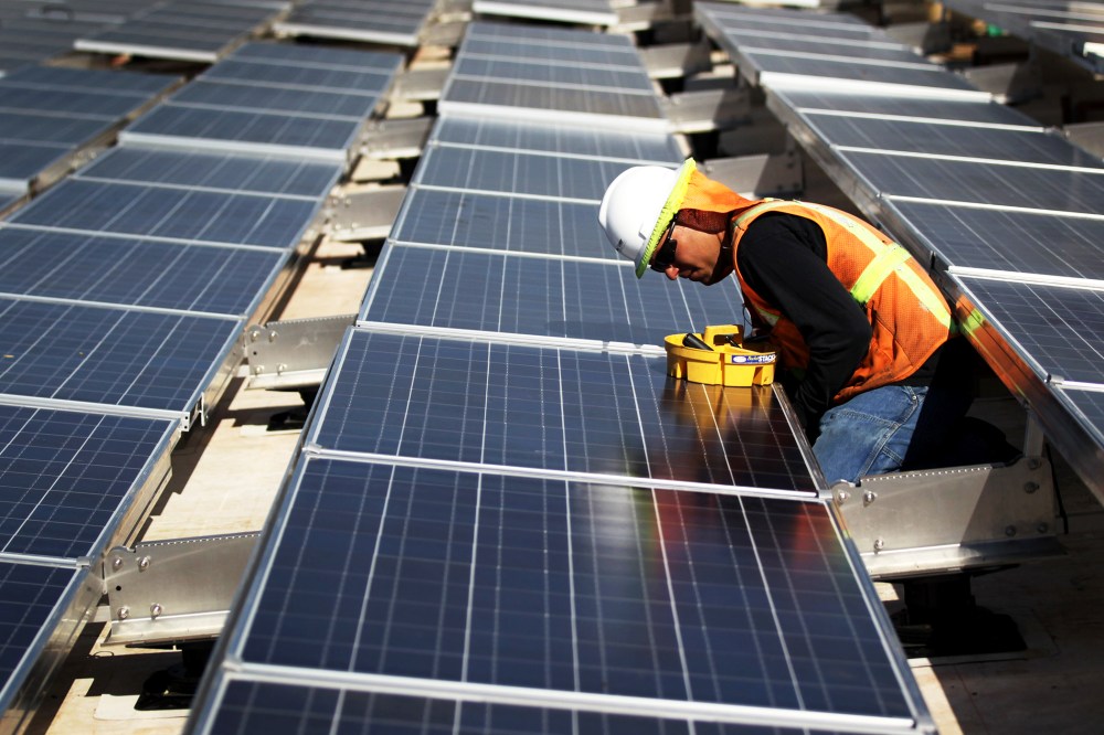 A worker finishes installing solar panels funded by federal stimulus funds atop a government building.