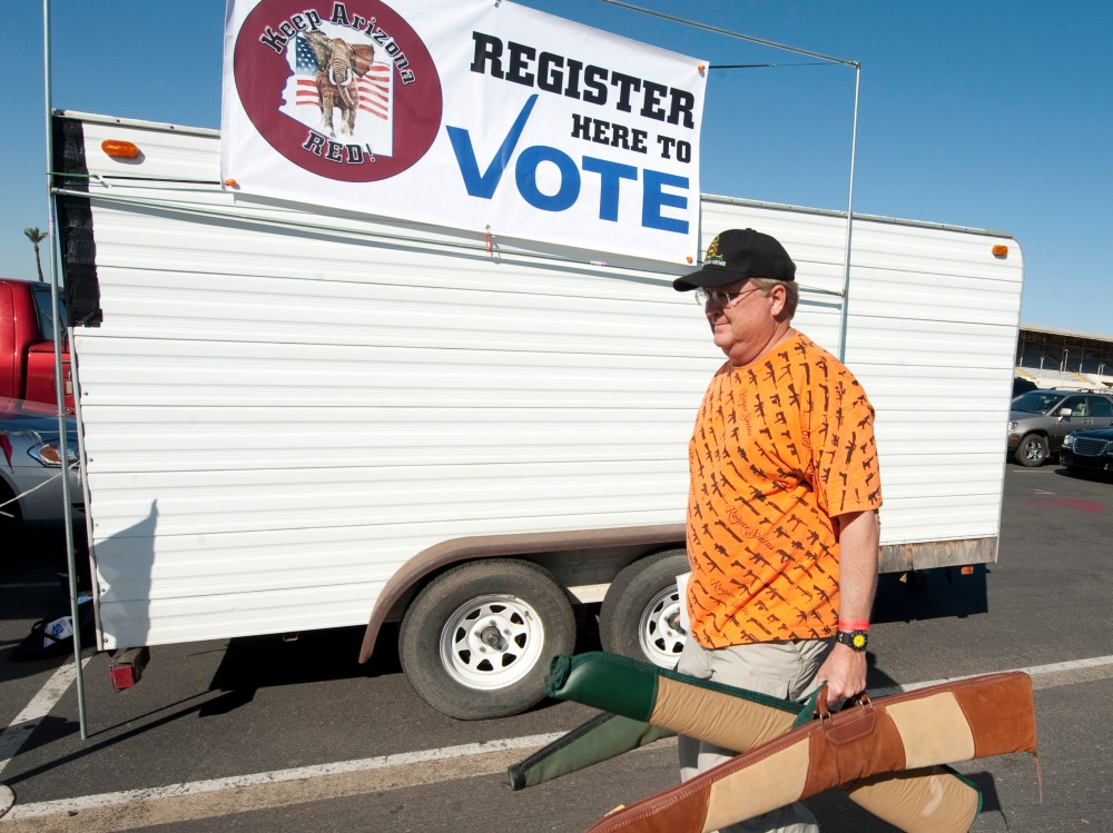 File Photo: A man carries his guns past a voter registration booth on his way to a gun show at the Arizona state fairgrounds  February 25, 2012 in Phoenix, Arizona. The Arizona and Michigan primaries are scheduled to be held February 28, 2012. (Photo...