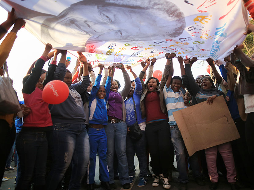 People dance and celebrate as they wave a banner of Nelson Mandela to celebrate his 95th birthday outside the Mediclinic Heart Hospital where he is being treated on July 18, 2013 in Pretoria, South Africa.   (Photo by Christopher Furlong/Getty Images)