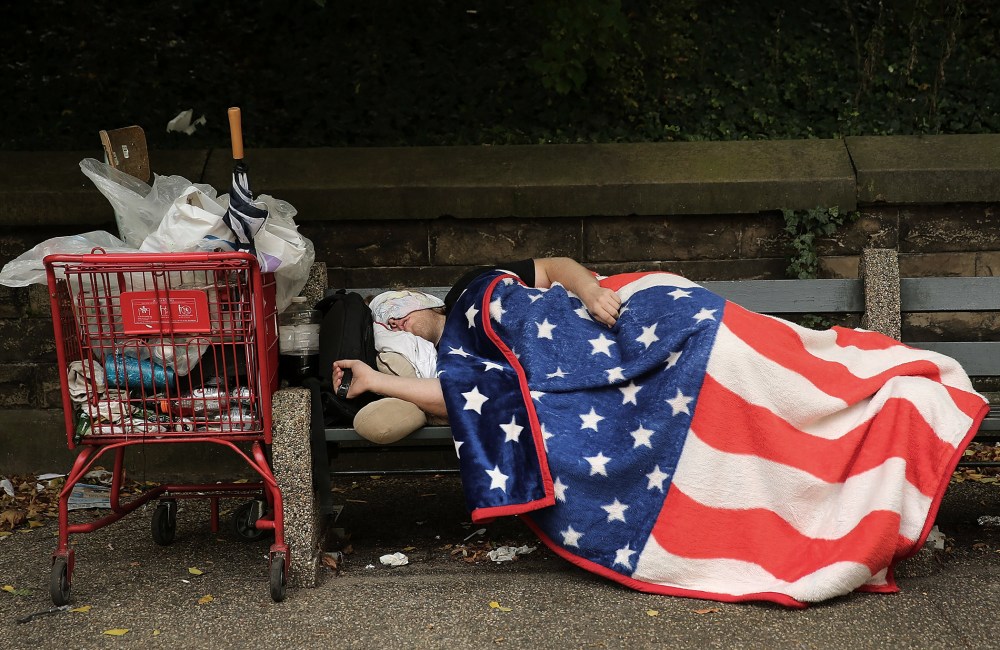 A homeless man sleeps under an American Flag blanket on a park bench on Sept. 10, 2013 in the Brooklyn borough of New York City.