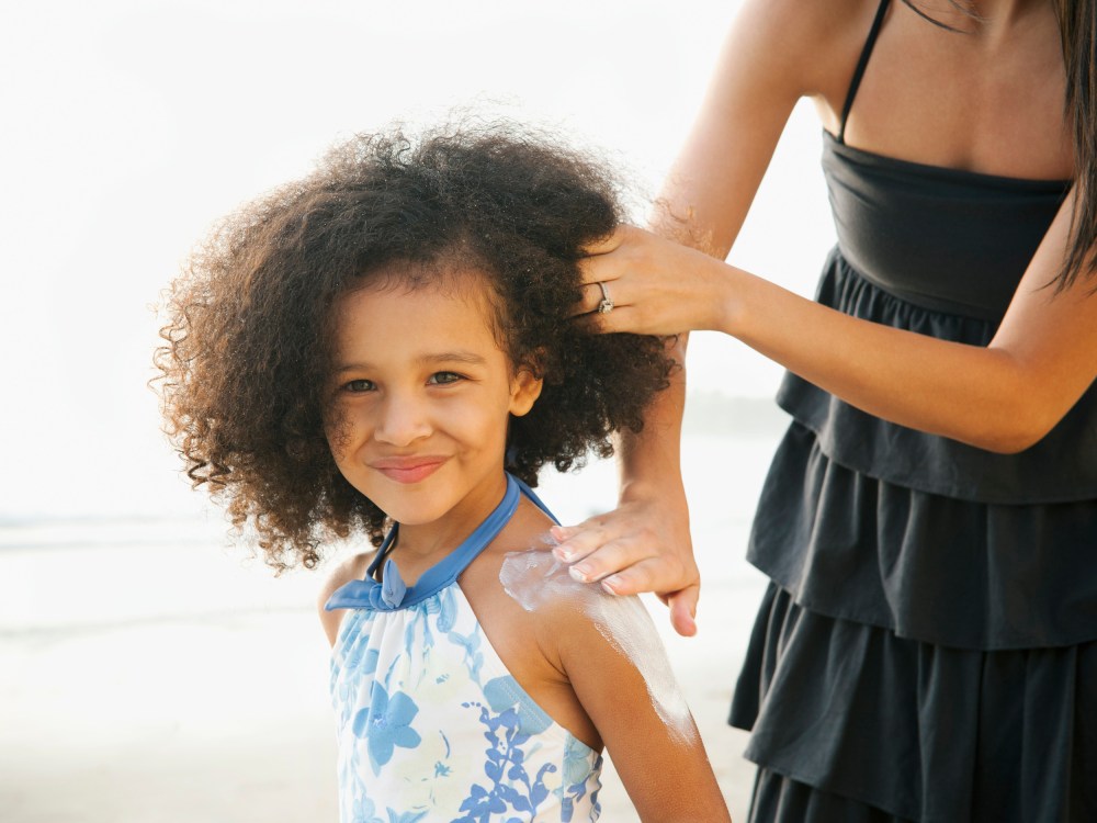 Image: Hispanic mother rubbing sunscreen on daughter at beach