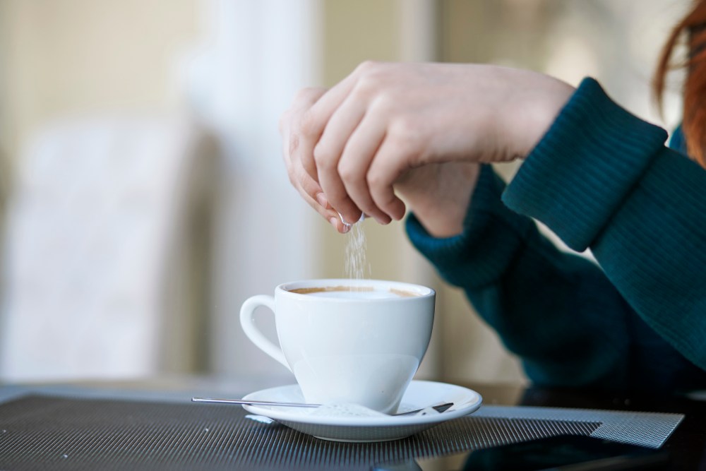 Woman pouring sugar into coffee