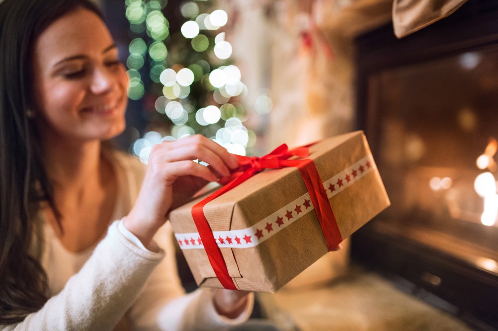 Woman in front of Christmas tree holding present.