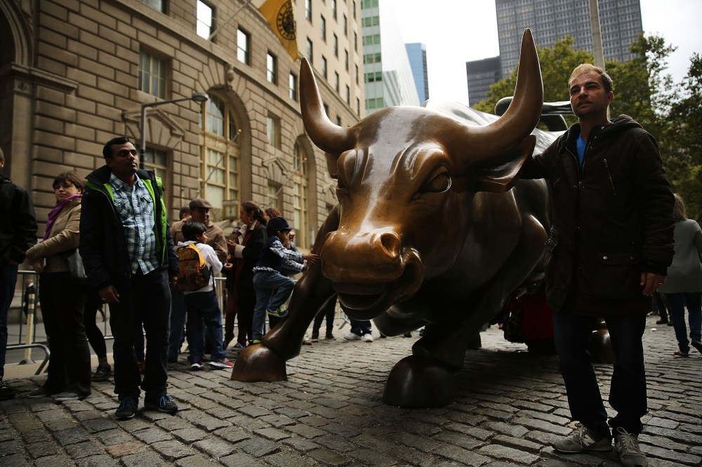 Pedestrians pass the bronze Charging Bull sculpture next to Wall Street in the Financial District on October 10, 2013 in New York City.