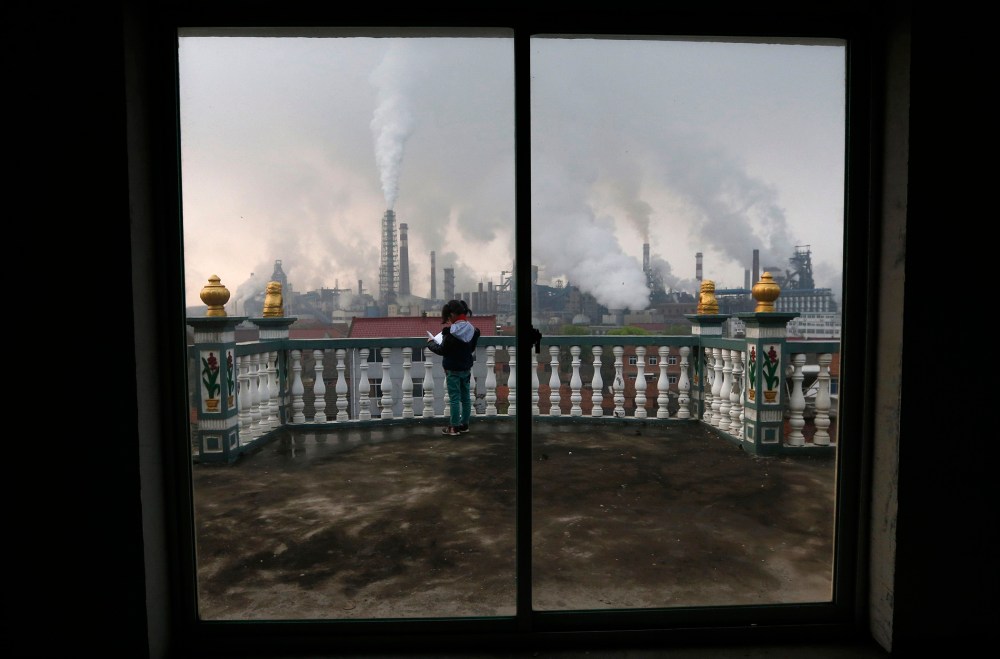 A girl reads a book on her balcony as smoke rises from chimneys of a steel plant, on a hazy day in Quzhou, Zhejiang province in this April 3, 2014 file photo.