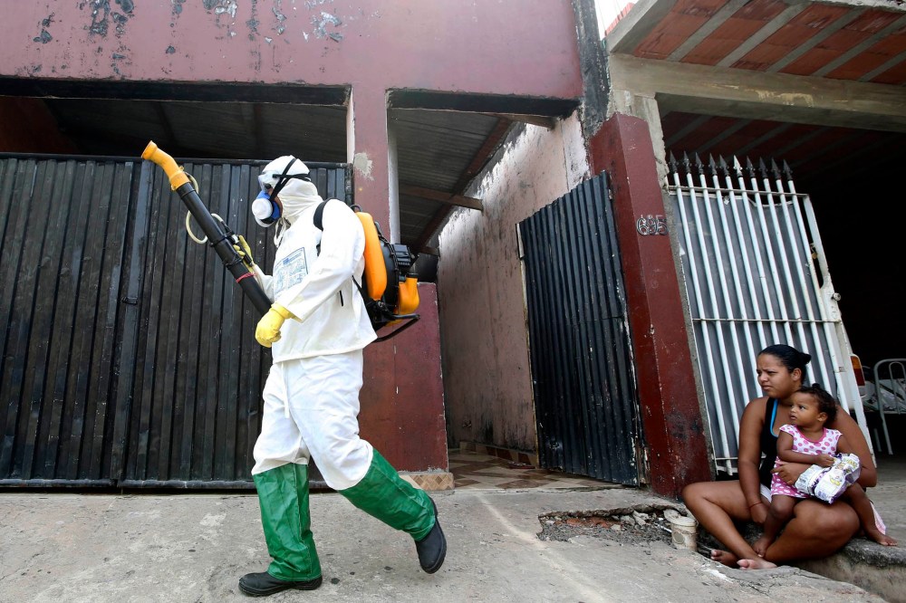 A national health official walks past residents as he carries out fumigation to help control the spread of dengue fever, which are caused by viruses carried by mosquitoes, in Rio Claro, Sao Paulo on March 6, 2015.