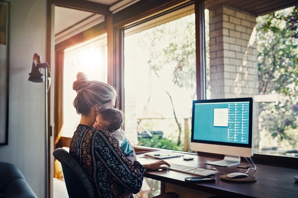 young woman working at home while holding her newborn baby son