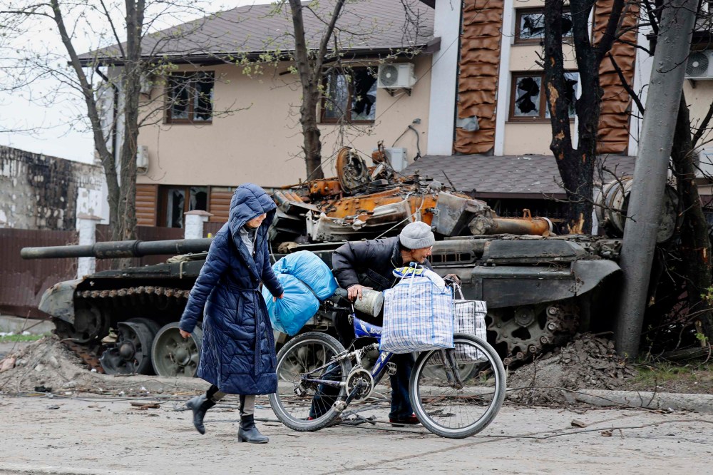 Local civilians walk past a tank destroyed during heavy fighting in an area controlled by Russian-backed separatist forces in Mariupol, Ukraine on Tuesday, April 19.
