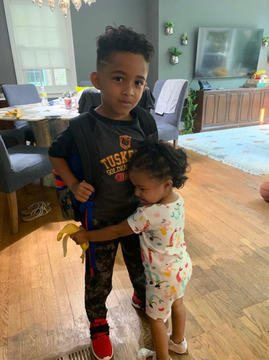 Image: A child wearing a backpack is hugged by a younger child.