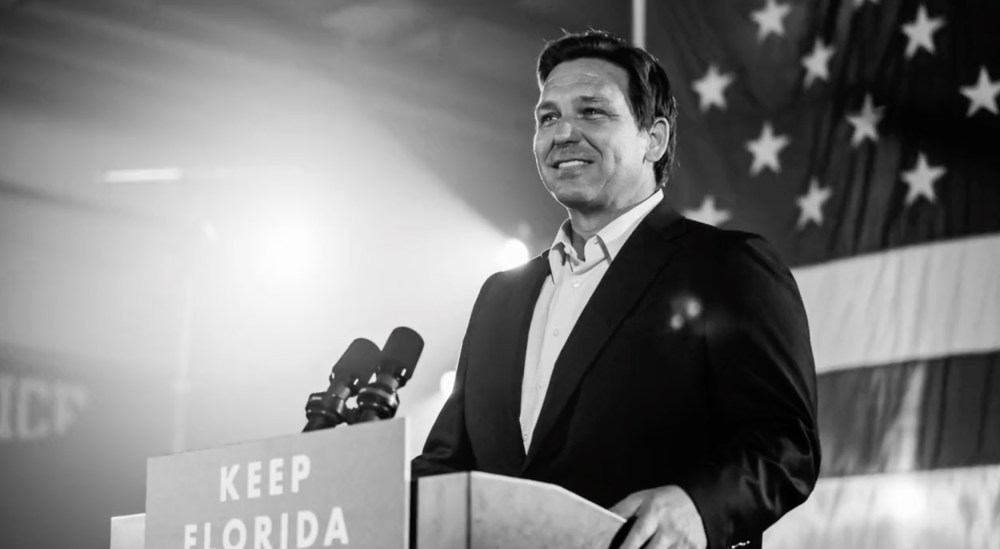 Image: Still from a campaign ad showing Ron DeSantis on a podium.
