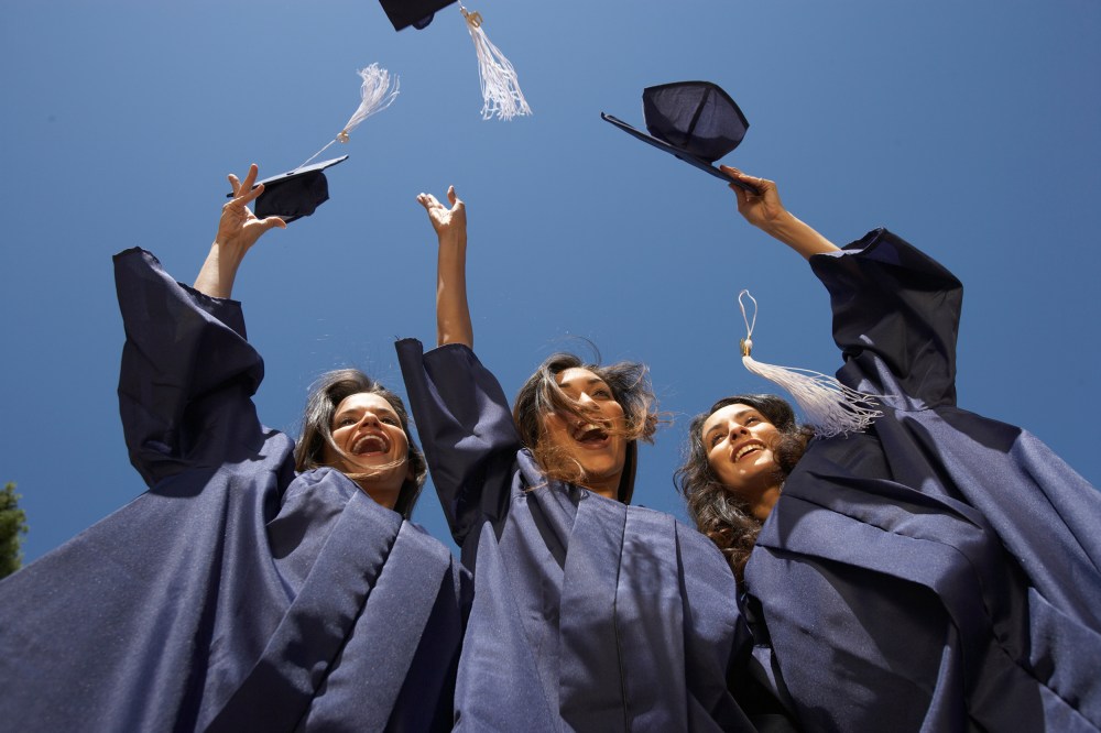 Three female graduate students throwing mortar boards, low angle view