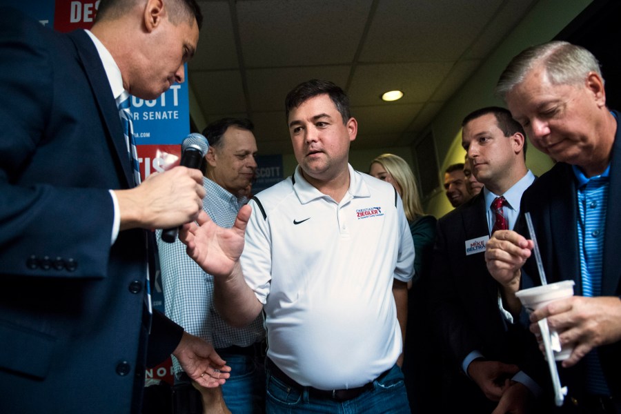 Christian Ziegler reaches for a microphone while surrounded by people
