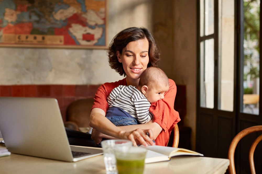 Mother carrying baby while reading book at table