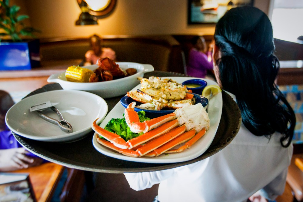 A waitress carries a tray a lobster kettle and a crab trio dish at a Red Lobster restaurant.