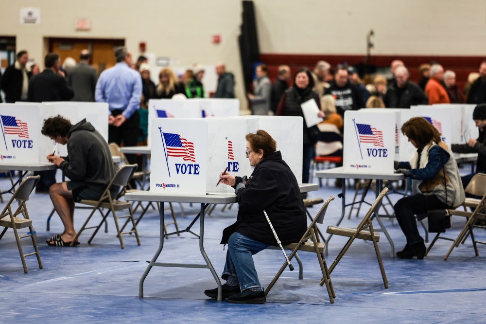 Voters fill out their ballots at a polling location behind dividers that say "Vote" with the American flag