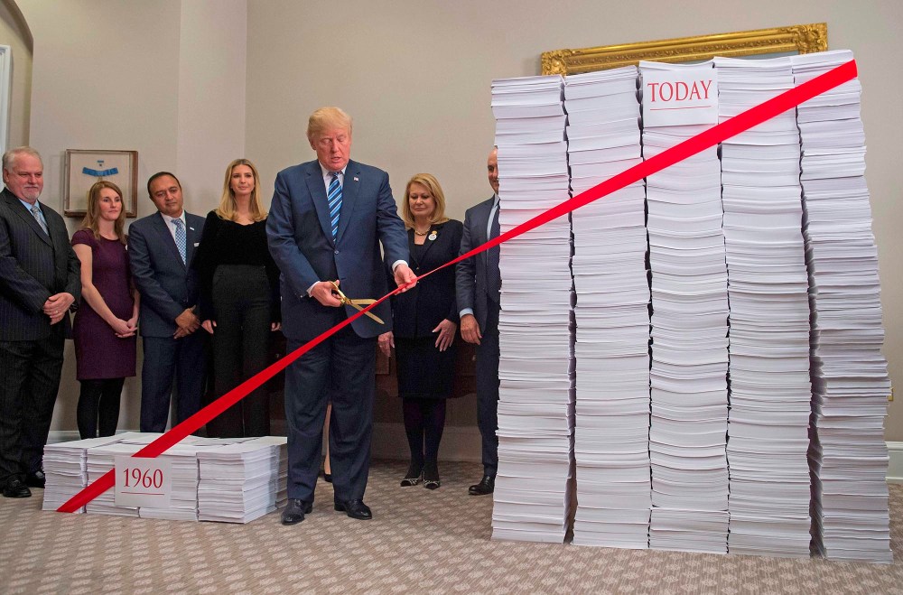 President Donald Trump uses gold scissors to cut red tape between  stacks of papers representing government regulations on Dec. 14, 2017, at the White House.