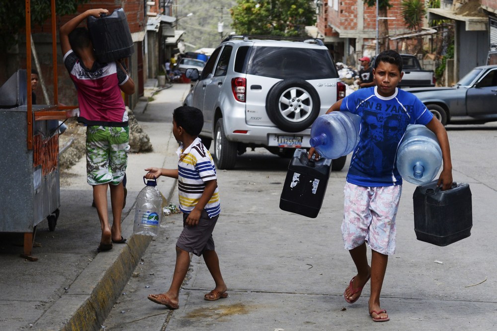 Boys carry empty bottles and cans to fill them with water in Caucaguita, Caracas, on June 20, 2014.