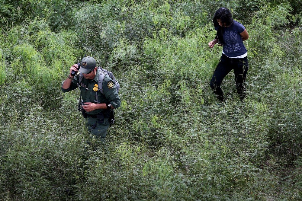 A U.S. Border Patrol escorts an undocumented immigrant, her arm handcuffed behind her back, after detaining her in the brush on Sept. 11, 2014 near Falfurrias, Texas.