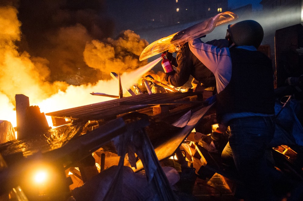 Anti-government protesters stand behing their burning barricades during clashes with police in the center of Kiev.