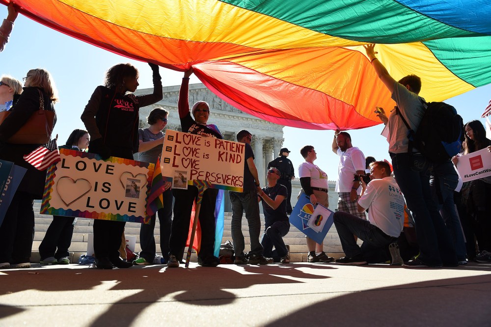 Supporters of gay marriage stand beneath a large rainbow flag which is placed in support of gay marriage in front of the U.S. Supreme Court in Washington, D.C., April 28, 2015. (Photo by Astrid Riecken/Washington Post/Getty)