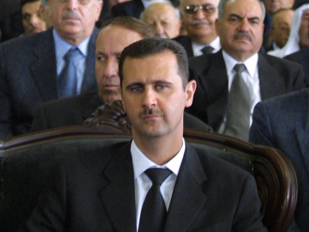 File Photo: Syrian President Bashar al-Assad (C) attends a ceremony marking the one-year anniversary his father's death in the northern city of Qerdaha 10 June 2001. (Photo by Louai Beshara/AFP/Getty Images File)