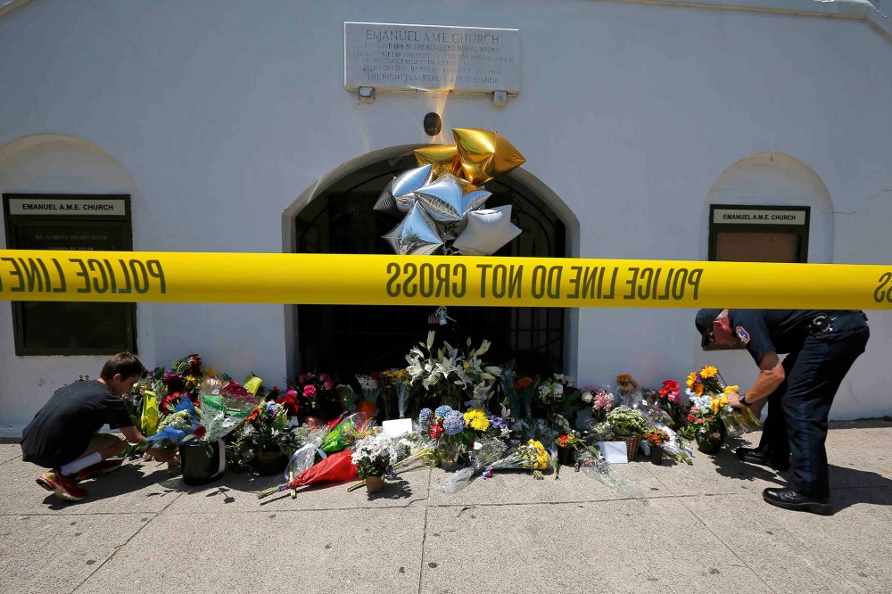 A boy helps a police officer move flowers left behind outside Emanuel African Methodist Episcopal Church after the street was re-opened a day after a mass shooting left nine dead at the church in Charleston, S.C. (Photo by Brian Snyder/Reuters)