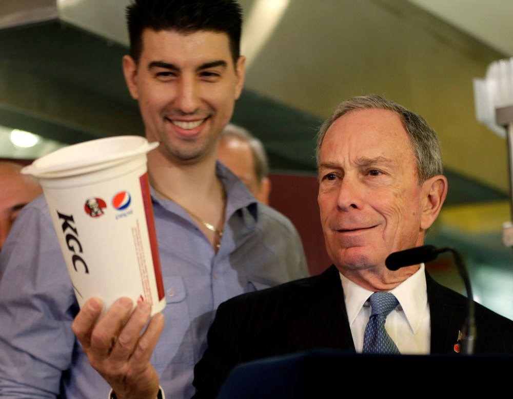 New York City Mayor Michael Bloomberg looks at a 64oz cup, as  Lucky's Cafe owner Greg Anagnostopoulos, left, stands behind him, during a news conference at the cafe in New York, Tuesday, March 12, 2013.  (AP Photo/Seth Wenig)