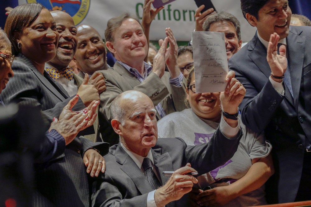 California Gov. Jerry Brown lifts a signed bill creating highest statewide minimum wage at $15 an hour by 2022 at the Ronald Reagan building in Los Angeles,April 4, 2016. (Photo by Nick Ut/AP)