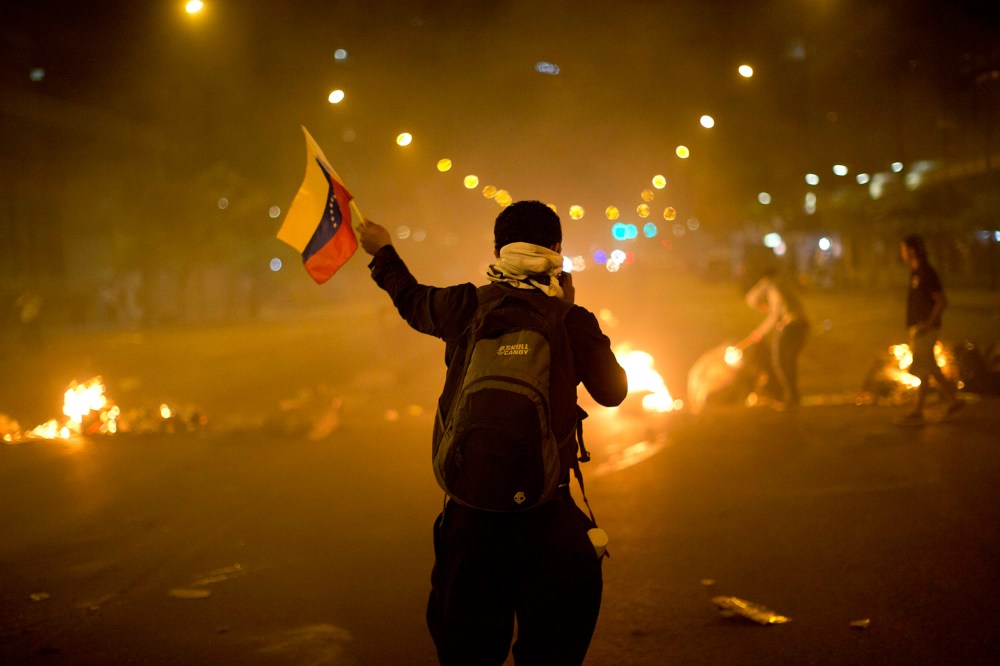 An anti-government demonstrator holds a representation of Venezuela's national flag in front of a burning barricade, Feb. 21, 2014, in the Altamira neighborhood of Caracas, Venezuela.