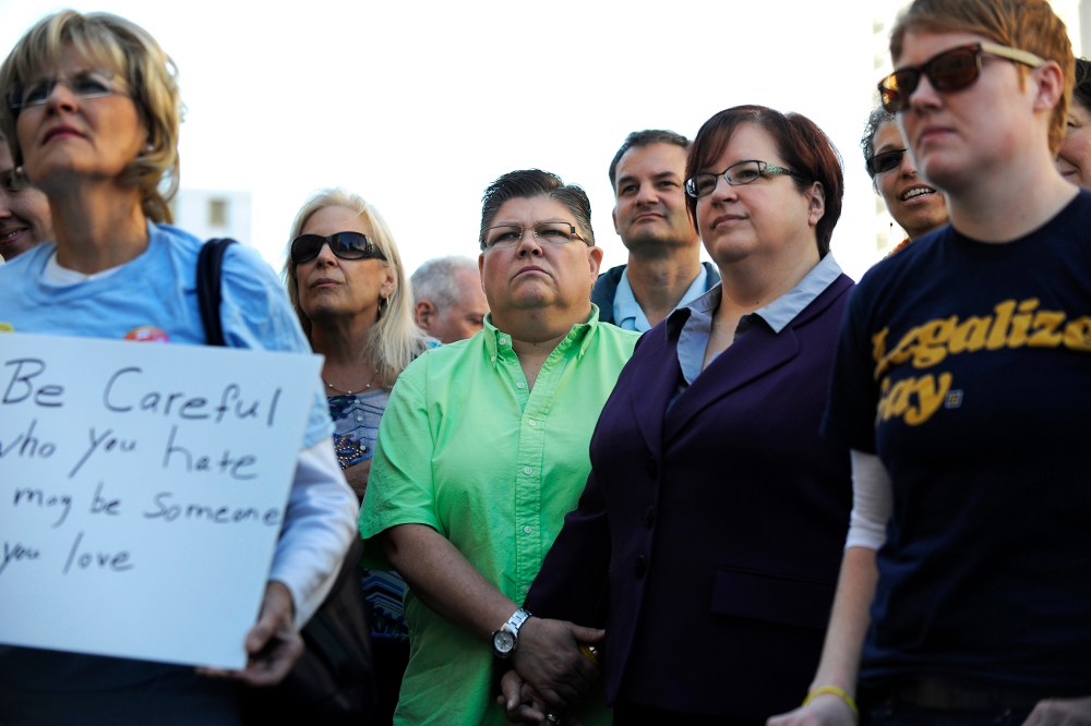 Same sex couple Jayne Rowse , green shirt, and April DeBoer hold hands during the rally outside the federal courthouse, Oct. 12, 2013, in Detroit, Mich.