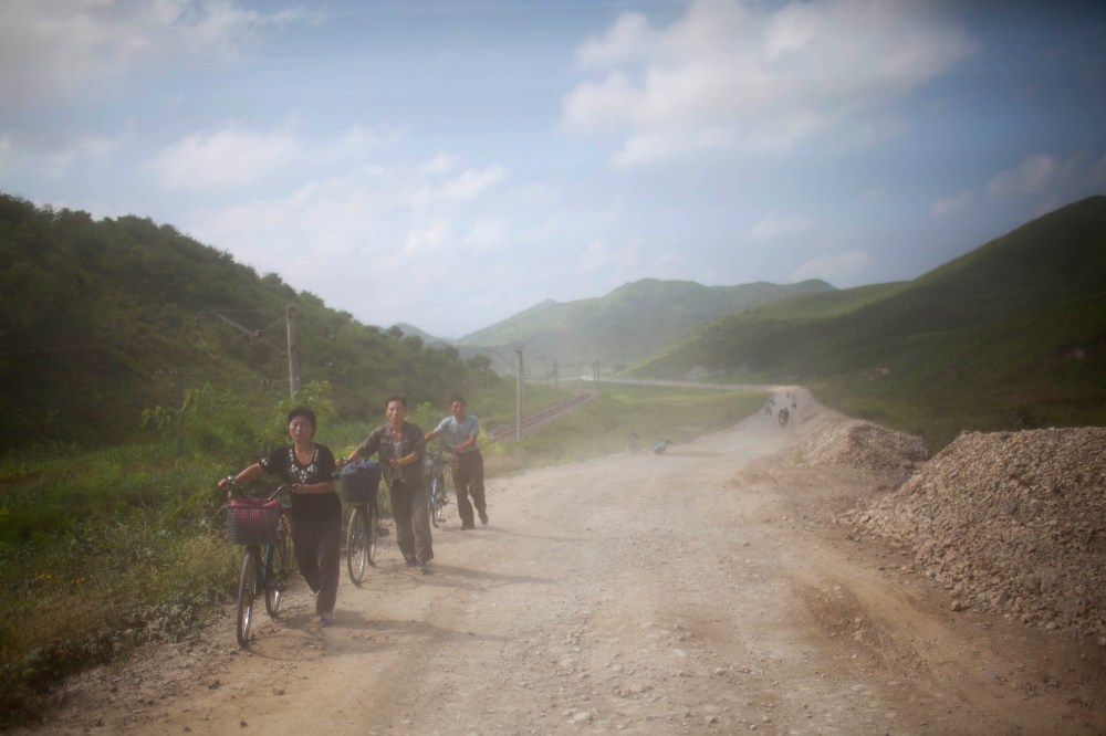 North Koreans are dusted by passing vehicles as they push their bicycles down a dirt road in Songchon County, North Korea on Aug 13, 2012.