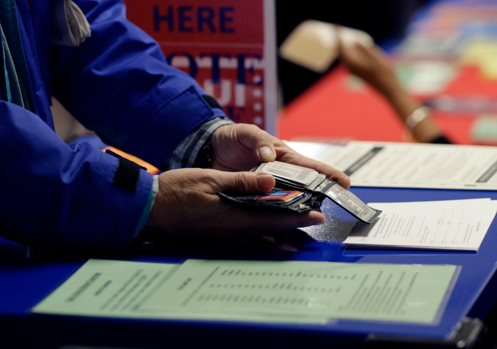 A voter shows his photo identification to an election official at an early voting polling site, in Austin, Texas, Feb. 26, 2014. (Photo by Eric Gay/AP)