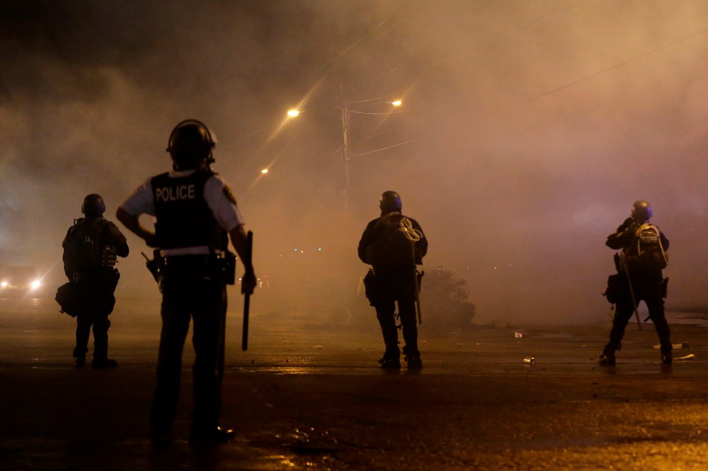 A law enforcement officer watches Sunday, Aug. 17, 2014, as tear gas is fired to disperse a crowd protesting the shooting of teenager Michael Brown last Saturday in Ferguson, Mo.