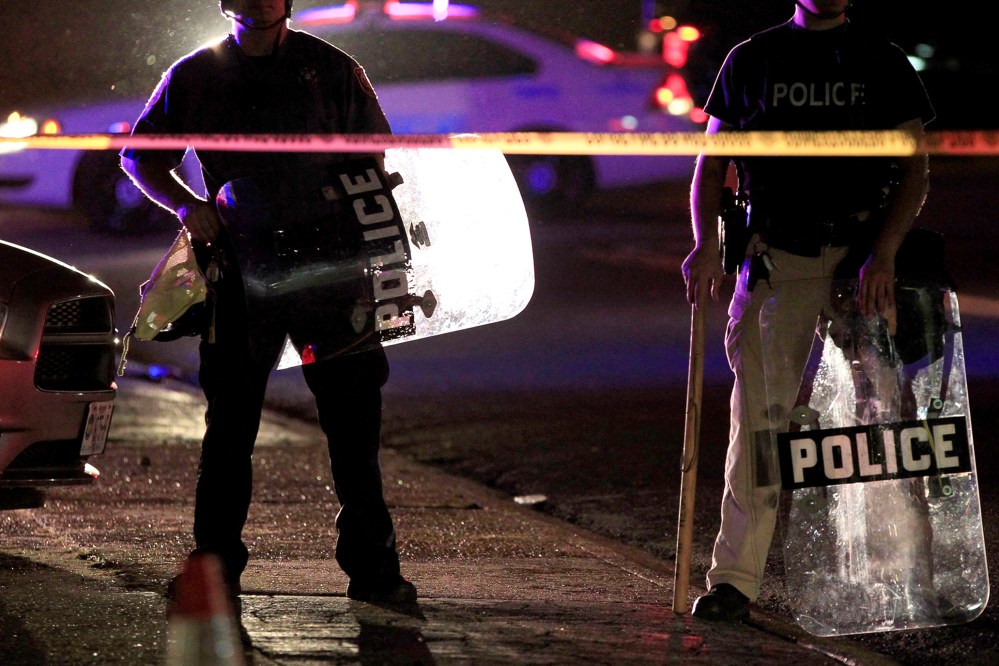 Police wearing riot gear stand at a post as they wait for a crowd to disperse Monday, Aug. 11, 2014, in Ferguson, Mo.