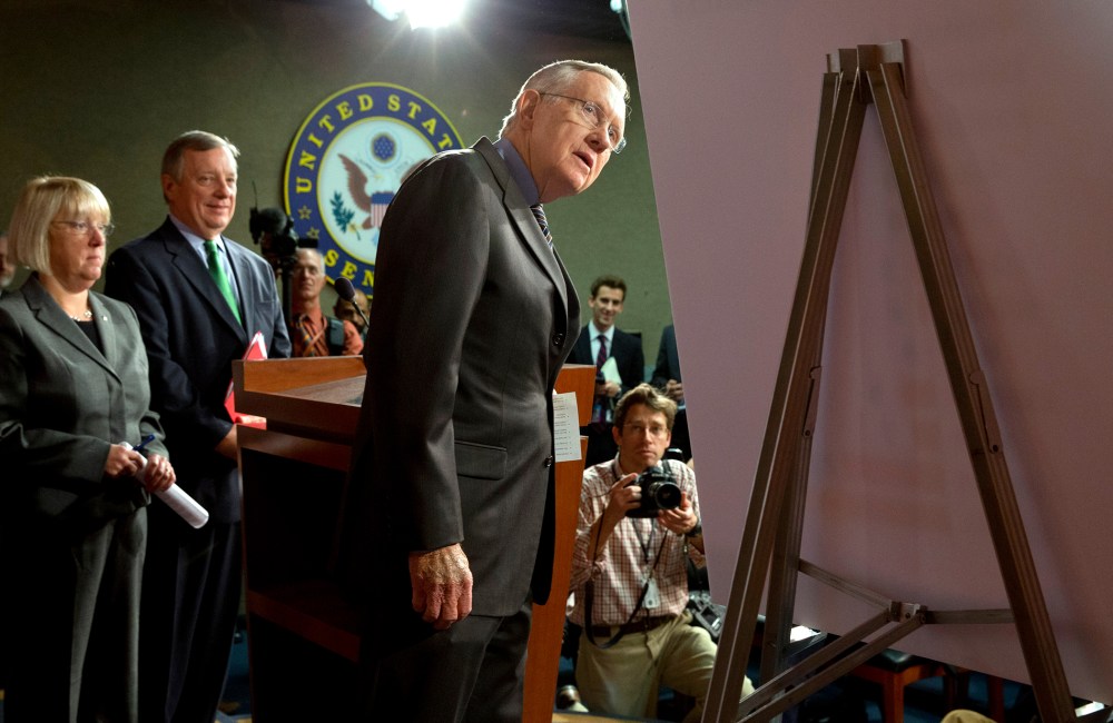 Senate Majority Leader Harry Reid of Nev., right, looks at a placard during a news conference in  Washington, on Nov. 21, 2013