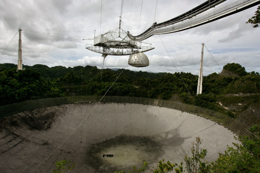 The superstructure up top and the dish below are the primary instruments of the world's largest radio telescope, currently undergoing a paintjob, near Arecibo, Puerto Rico, May 31, 2007. (Photo by Brennan Linsley/AP)