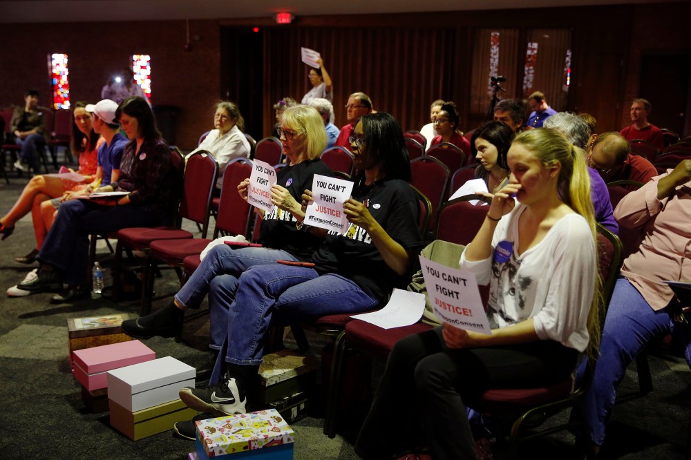 In this March 15, 2016 file photo, people watch and hold signs as members of the Ferguson City Council meet in Ferguson, Mo. (Photo by Jeff Roberson/AP)