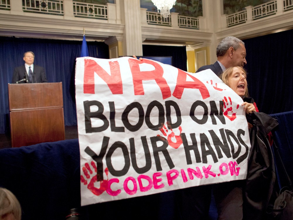 Activist Medea Benjamin, of Code Pink, is led away by security as she protests during a statement by National Rifle Association executive vice president Wayne LaPierre, left, during a news conference in response to the Connecticut school shooting on...