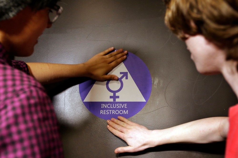 Two students place a new sticker on the door at the ceremonial opening of a gender neutral bathroom at Nathan Hale High School on May 17, 2016 in Seattle, Wash. (Photo by Elaine Thompson/AP)