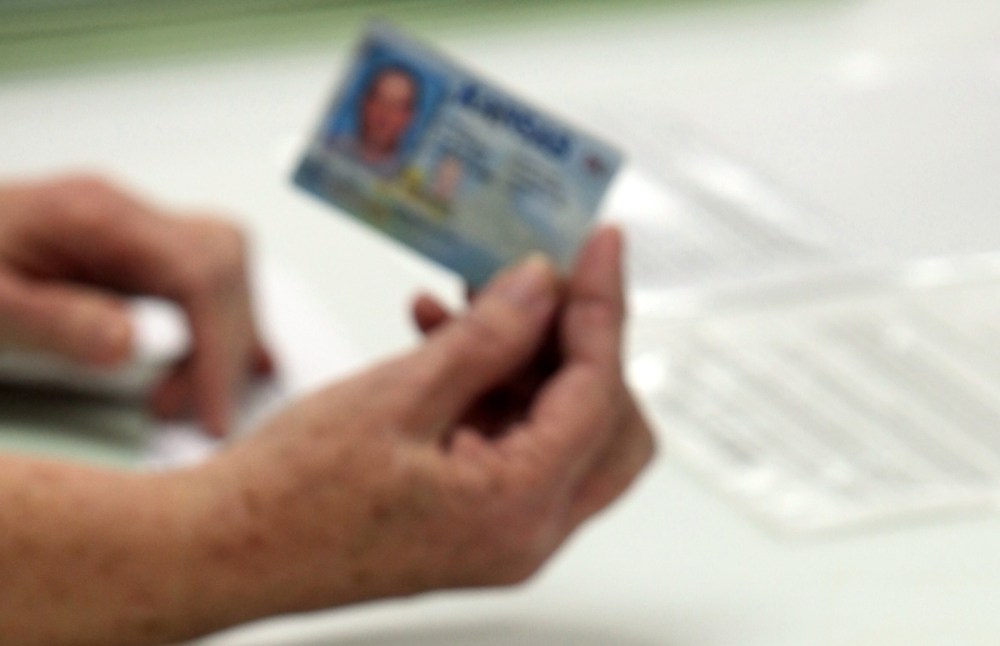 FILE - In this Jan. 10, 2012 file photo, election officials check the photo identification card of a voter in Cimarron, Kan. Voter ID laws designed to deter fraud may end up blocking thousands of legitimate ballots. (AP Photo/The The Hutchinson News,...