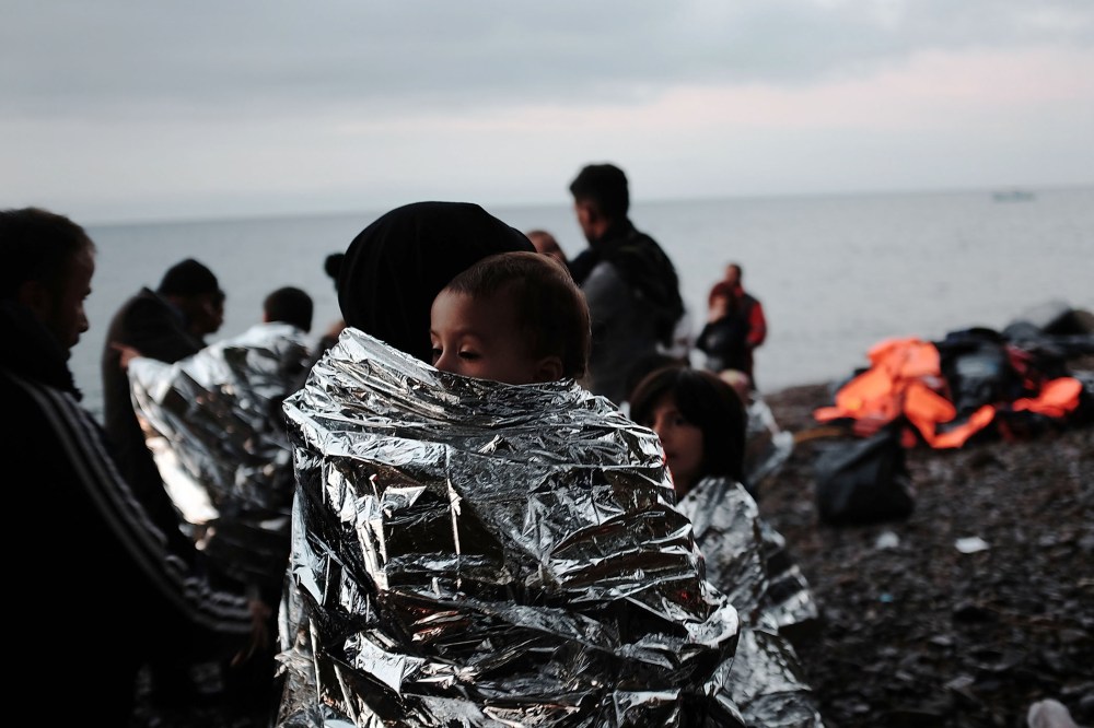 A group of migrants huddle on the beach after arriving by raft from Turkey onto the island of Lesbos on Oct. 21, 2015 in Sikaminias, Greece. (Photo by Spencer Platt/Getty)
