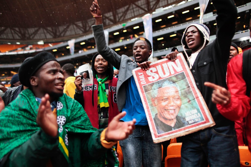 Supporters of late South African president Nelson Mandela sing and dance in the rain as they arrive to attend the memorial service in Johannesburg, Dec. 10, 2013.